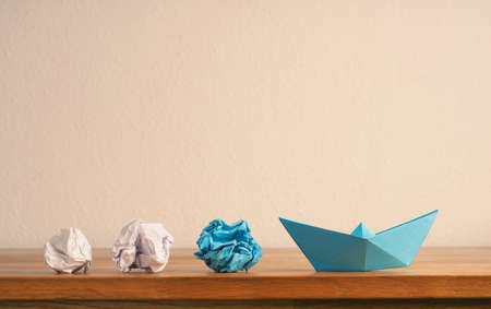 Teamwork business concept with crumpled paper and a paper boat on a wooden office table with space for textの写真素材