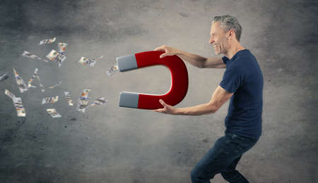 Happy man with a big magnet attracting money, abundance or wealth conceptの写真素材