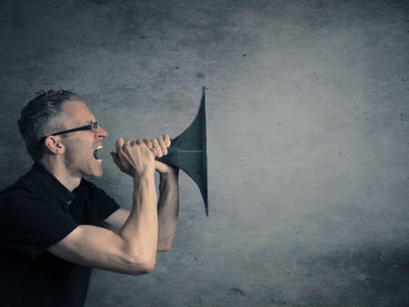 Young man holding a big horn, speaking loud concept on a dark studio background with space for text...