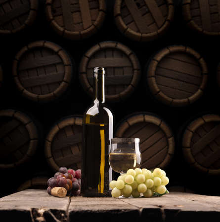 Bottle of white wine with grapes on a rustic table in the wine cellar, Concept for viticulture,...
