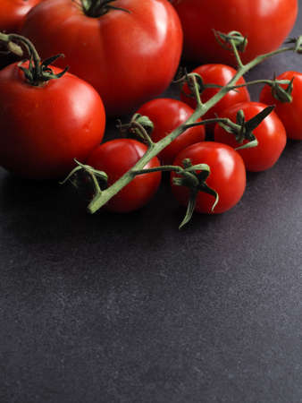 Different organic tomato varieties on a dark stone kitchen table with space for text or imageの写真素材