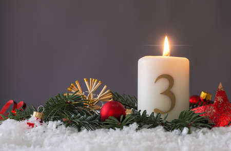 Candle of the third Advent burns, fir branches and Christmas tree balls in the snow, seasonal or holiday conceptの写真素材