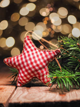 Homemade cloth star with fir branches on a wooden table in front of a Christmas tree bokeh. Seasonal...