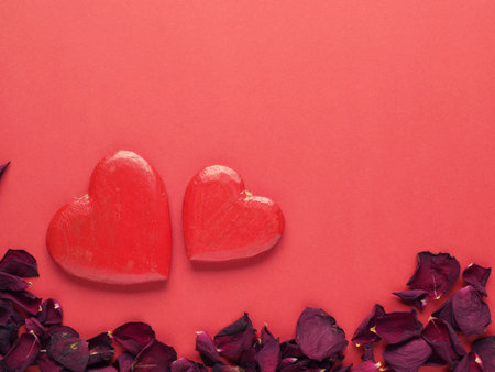 Rustic wooden hearts with rose petals on red background with space for textの写真素材