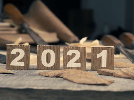 Wooden blocks with Year 2021 on a rustic workbench with chisels, wood working or creativity concept with space for textの写真素材