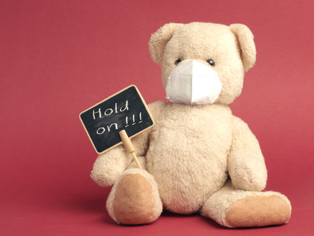 Teddy bear with protective mask holds sign with inscription "Hang on!", Lock down pandemic Covid-19 conceptの写真素材