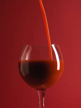 Pouring fresh organic tomato juice in a glass, red background, healthy food and drink conceptの写真素材