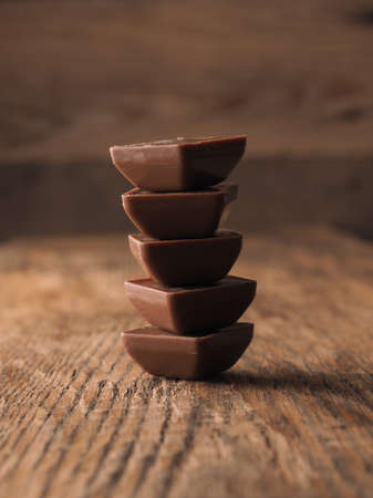 A pile of chocolate pieces on a rustic wooden table, unhalthy food, caloriesの写真素材