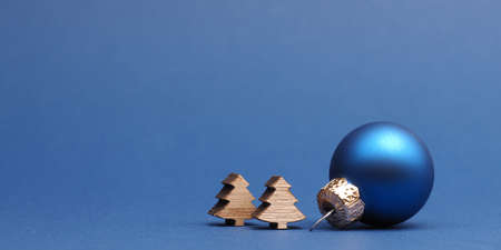 Blue Christmas tree ball with small wooden tree shapes on a blue paper background with space for your textの写真素材