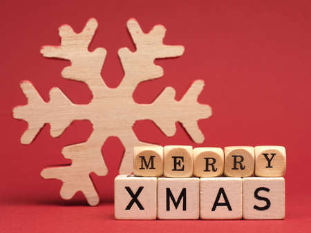 Wooden blocks with the words Merry Christmas and a snowflake shape on a red background, space for textの写真素材