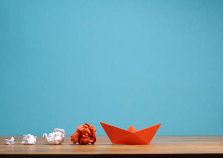 Teamwork business concept with crumpled paper and a paper boat on a wooden office table with space...