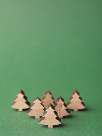 Small wooden Christmas tree shapes on a green paper background with space for your textの写真素材