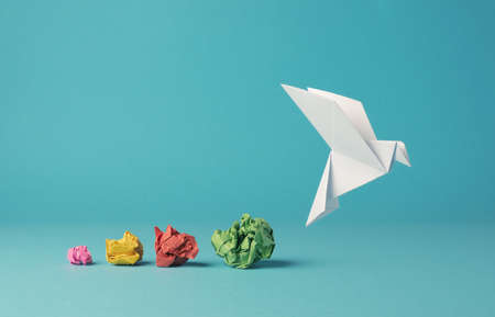 Colorful crumpled paper balls with an origami paper dove, peace, freedom, diversity or opportunity concept on a blue backgroundの写真素材