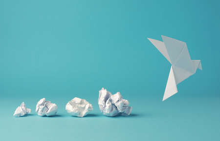 Crumpled paper balls with an origami paper dove, peace, freedom or opportunity concept on a blue backgroundの写真素材