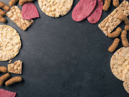 Organic crackers from lentils, beet, nuts and corn as a frame on a stone background, space for your textの写真素材