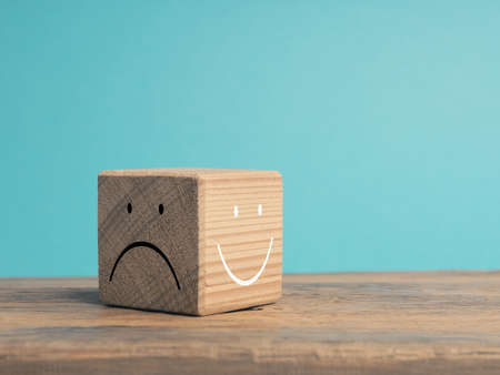 A wooden cube with light and dark side, once with smiling face and with sad face, There is always the option to choose, which face do you choose?の写真素材