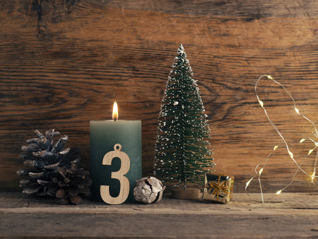 Candle of the third Advent burns, pine cones and Christmas decoration on wood with Christmas lightsの写真素材