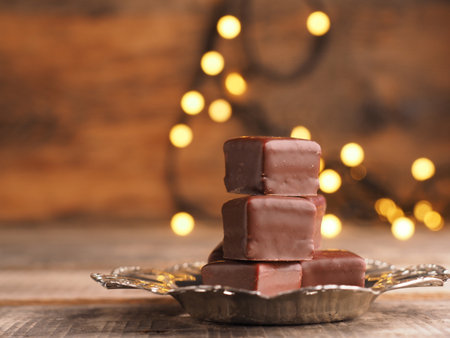 Stacked chocolate dices on a silver plate on a wooden table with Christmas lightsの写真素材