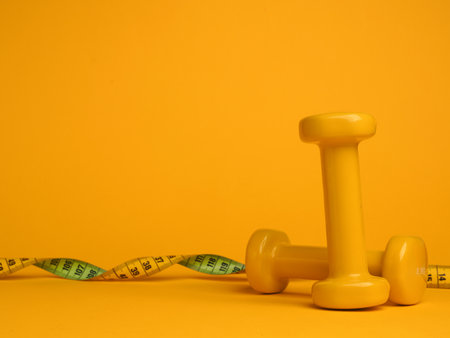 Yellow dumbbells with a tape measure on a yellow background, space for your text, fitness or diet conceptの写真素材