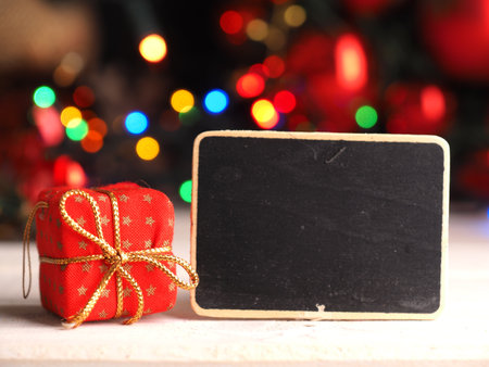 Red gift box with a small blackboard and blurred Christmas lights in the backgroundの写真素材