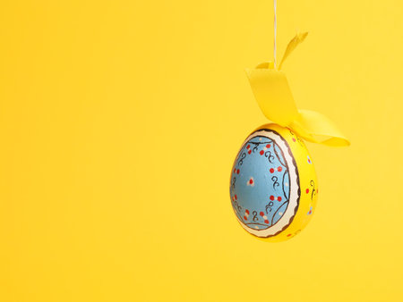 Hand-painted Easter egg with a bow on a yellow background, Easter greetingsの写真素材