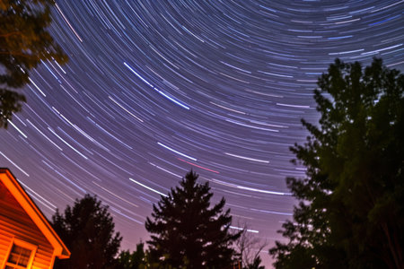 star trails in the night sky over a house and treesの素材