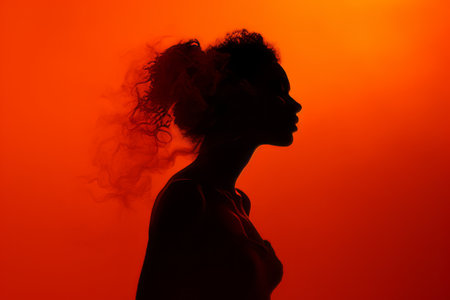 silhouette of a woman with smoke coming out of her hair on an orange backgroundの素材