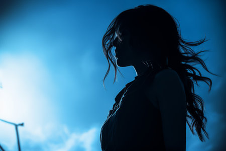 a silhouette of a woman standing in front of a blue skyの素材