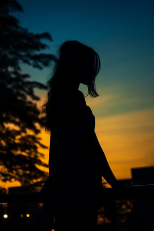 a silhouette of a woman standing on a balcony at sunsetの素材
