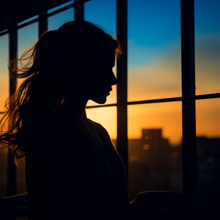 a silhouette of a woman looking out a window at sunsetの素材
