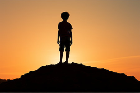 silhouette of a boy standing on top of a hill at sunsetの素材