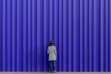 a woman wearing a striped shirt and hat stands in front of a blue wallの素材