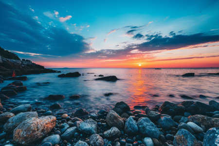 a beautiful sunset over the ocean with rocks on the shoreの素材