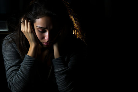 a woman sitting in the dark with her hands on her headの素材