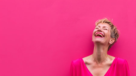 a woman laughing and smiling against a bright pink wallの素材