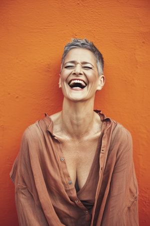 a woman with short hair laughing in front of an orange wallの素材