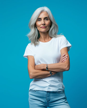 an older woman in a white t - shirt and jeans standing against a blue backgroundの素材