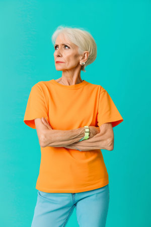 an older woman in an orange t - shirt and blue jeans standing against a turquoise backgroundの素材