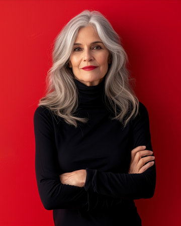 a woman with gray hair and a black turtleneck standing in front of a red wallの素材
