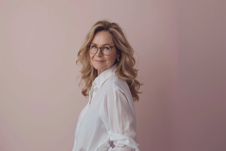 a woman with glasses and a white shirt standing in front of a pink wallの素材