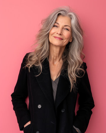 an older woman with gray hair posing against a pink backgroundの素材
