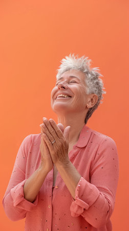happy senior woman clapping her hands on an orange backgroundの素材