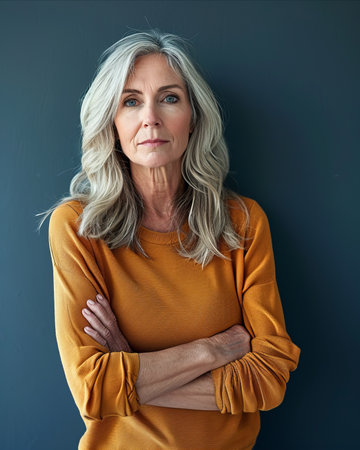 an older woman with gray hair and a yellow sweater standing in front of a gray wallの素材