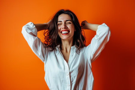 portrait of a happy young woman with her hands on her head against an orange backgroundの素材