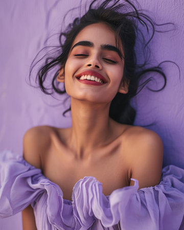 portrait of a beautiful young indian woman smiling against a purple wall stock photoの素材