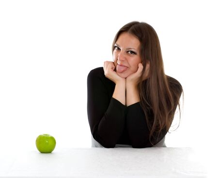 girl sitting at the table with green apple and showing tongueの写真素材