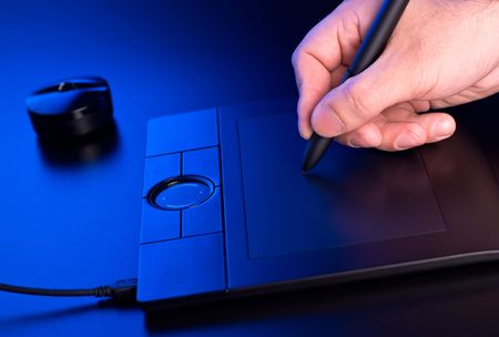 man's hand draws on graphic tablet in blue lightの写真素材