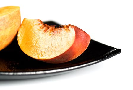 red peaches slices on black dish isolated on whiteの写真素材