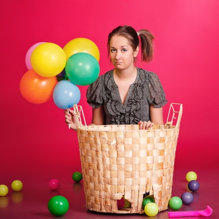 funny girl with basket of toys and balloons, red backgroundの写真素材