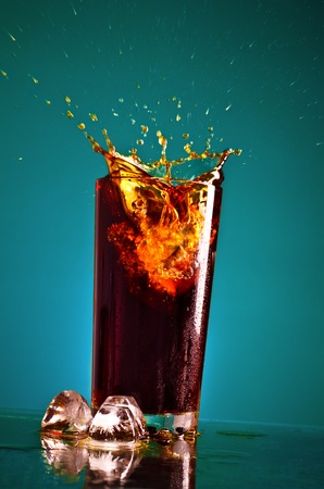 glass with splashing cola on blue backgroundの写真素材